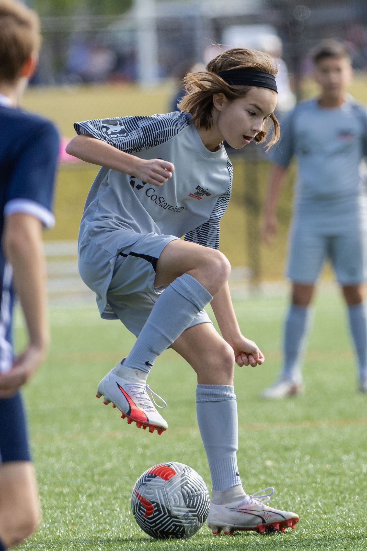 Youth soccer player in grey uniform performs skillful footwork with a ball during a match.