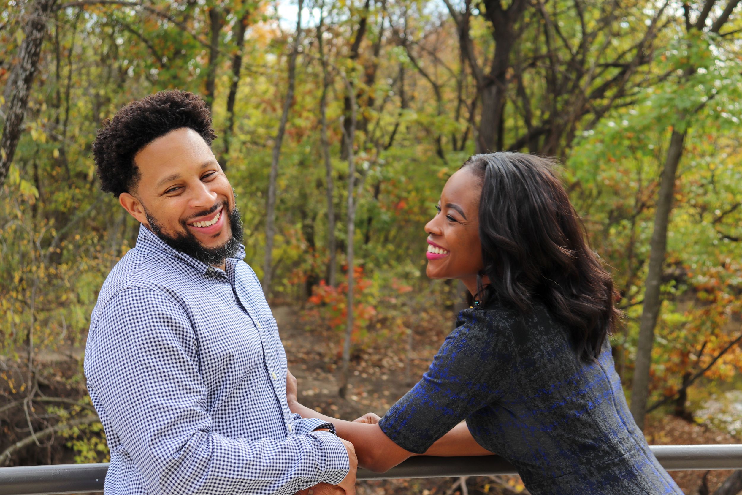 Couple laughing together on outdoor deck during autumn photoshoot.