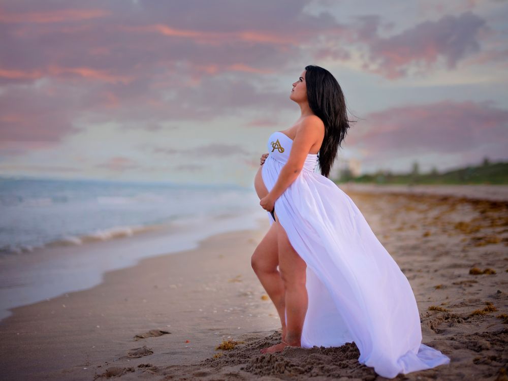 Silhouette of expectant figure in white dress against dramatic beach sunset.