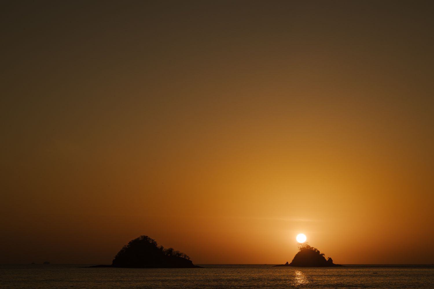 Dramatic orange sunset over calm ocean waters with silhouetted islands on the horizon.