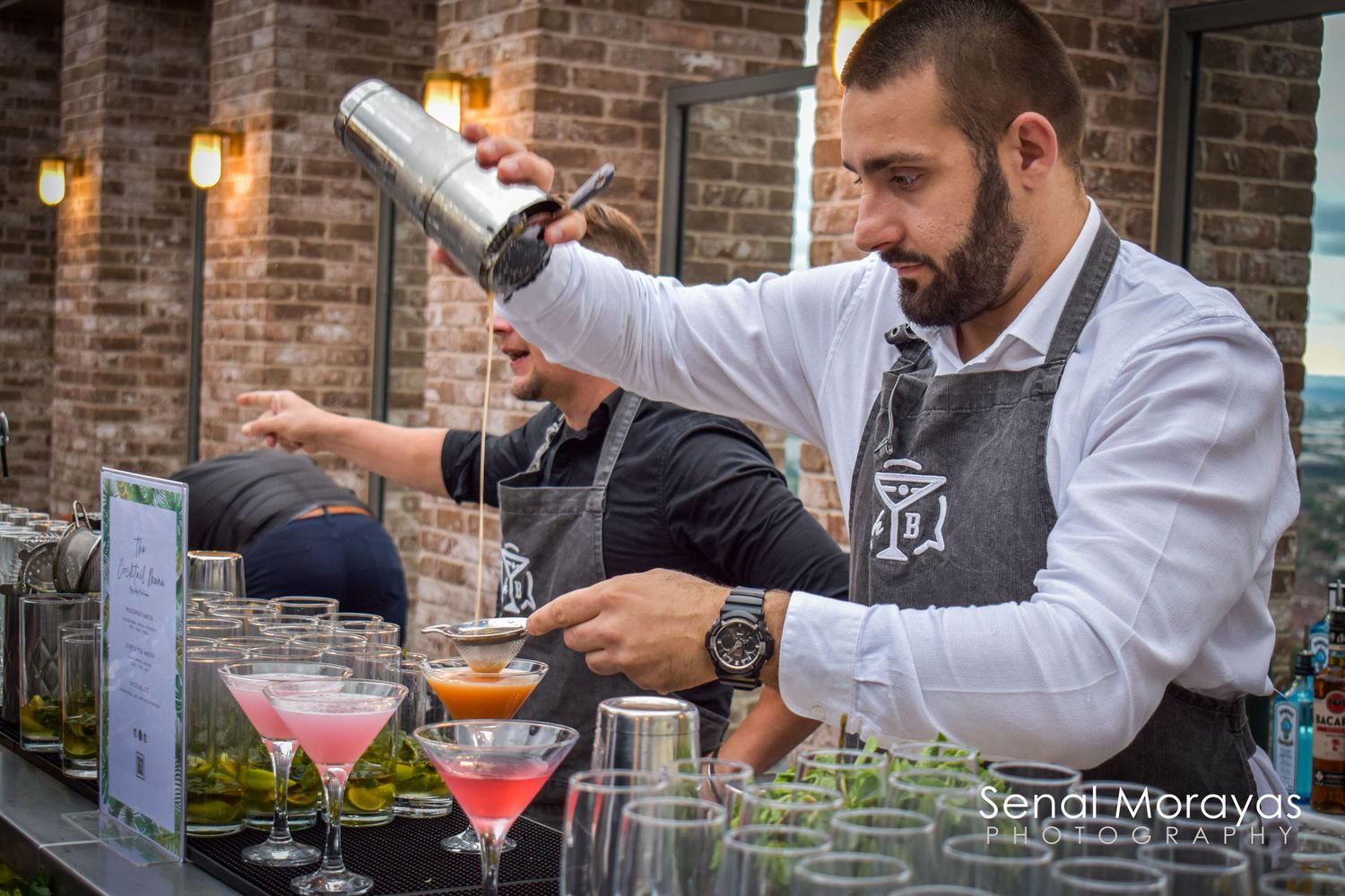 Professional bartenders preparing cocktails at a brick-walled venue.