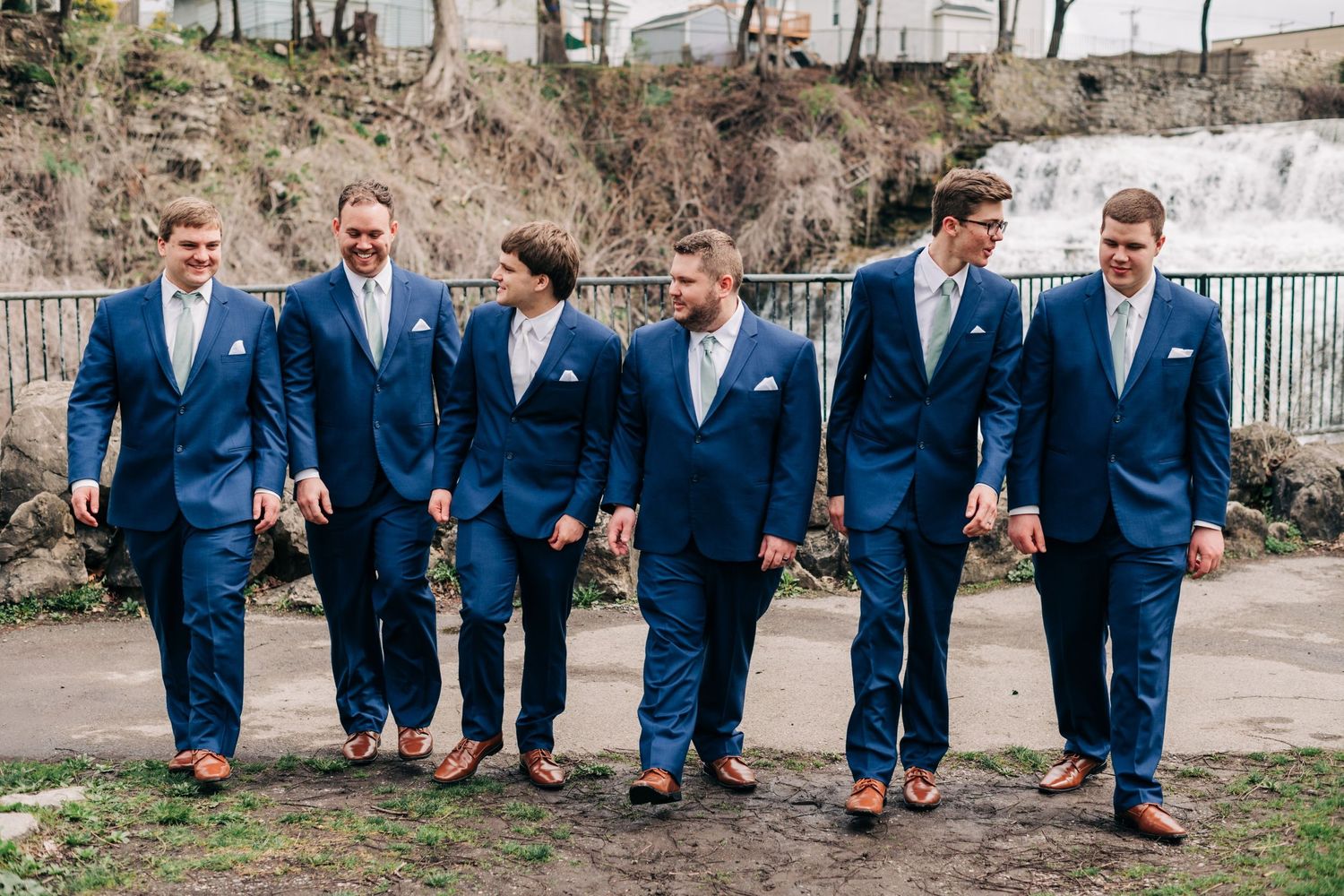groom and groomsmen in navy suits posing for portraits in front of a waterfall