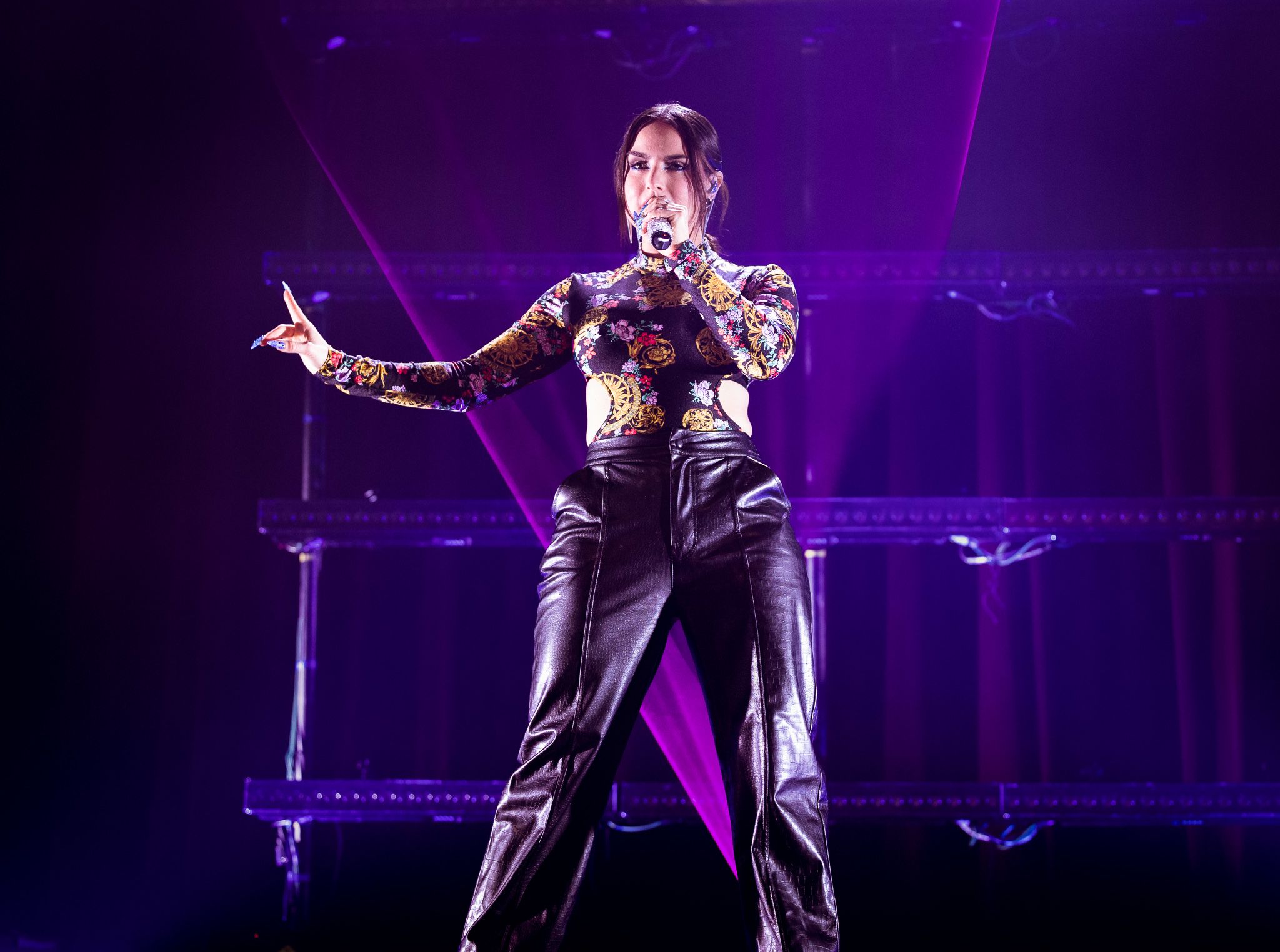 Performer in patterned top strikes dynamic pose against purple concert lighting.