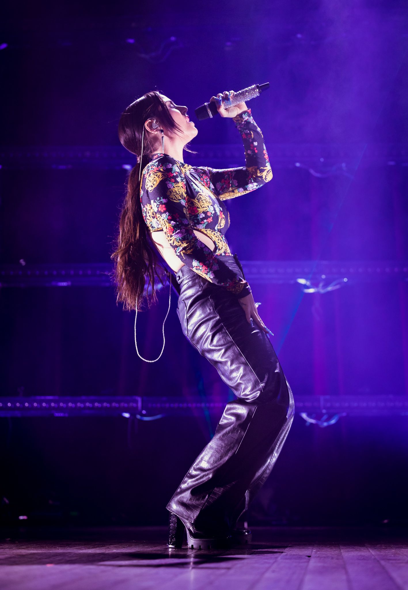 Performer in metallic outfit singing on stage with purple lighting and theatrical smoke effects.