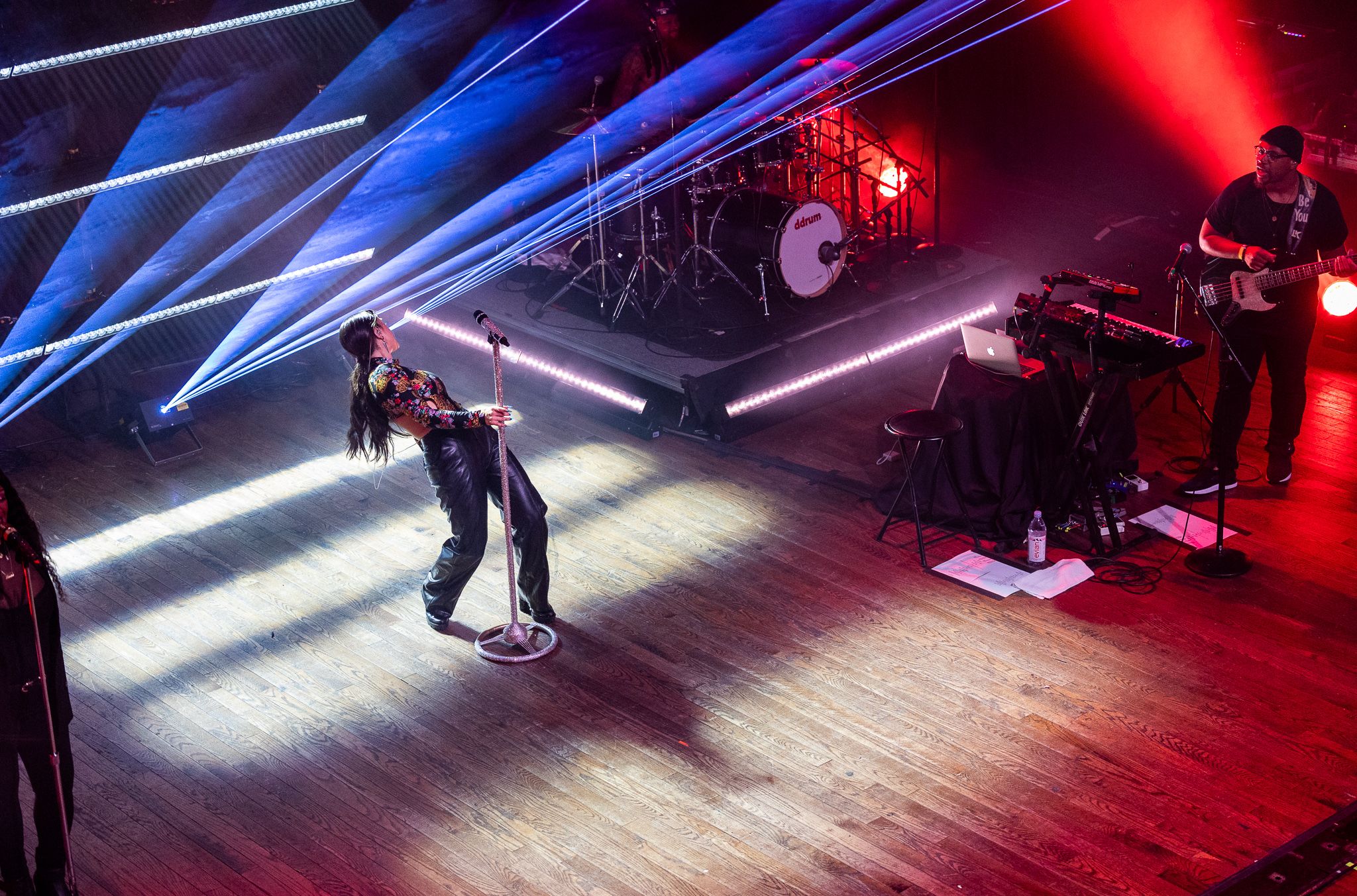 Concert performer on wooden stage with dramatic blue and red lighting effects.