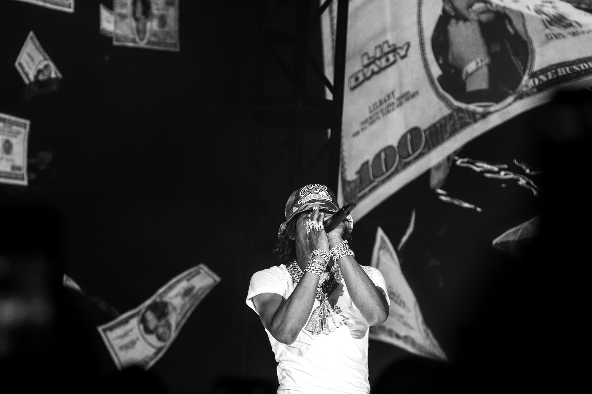 Concert performer in black and white with money visuals projected in background during stage show.