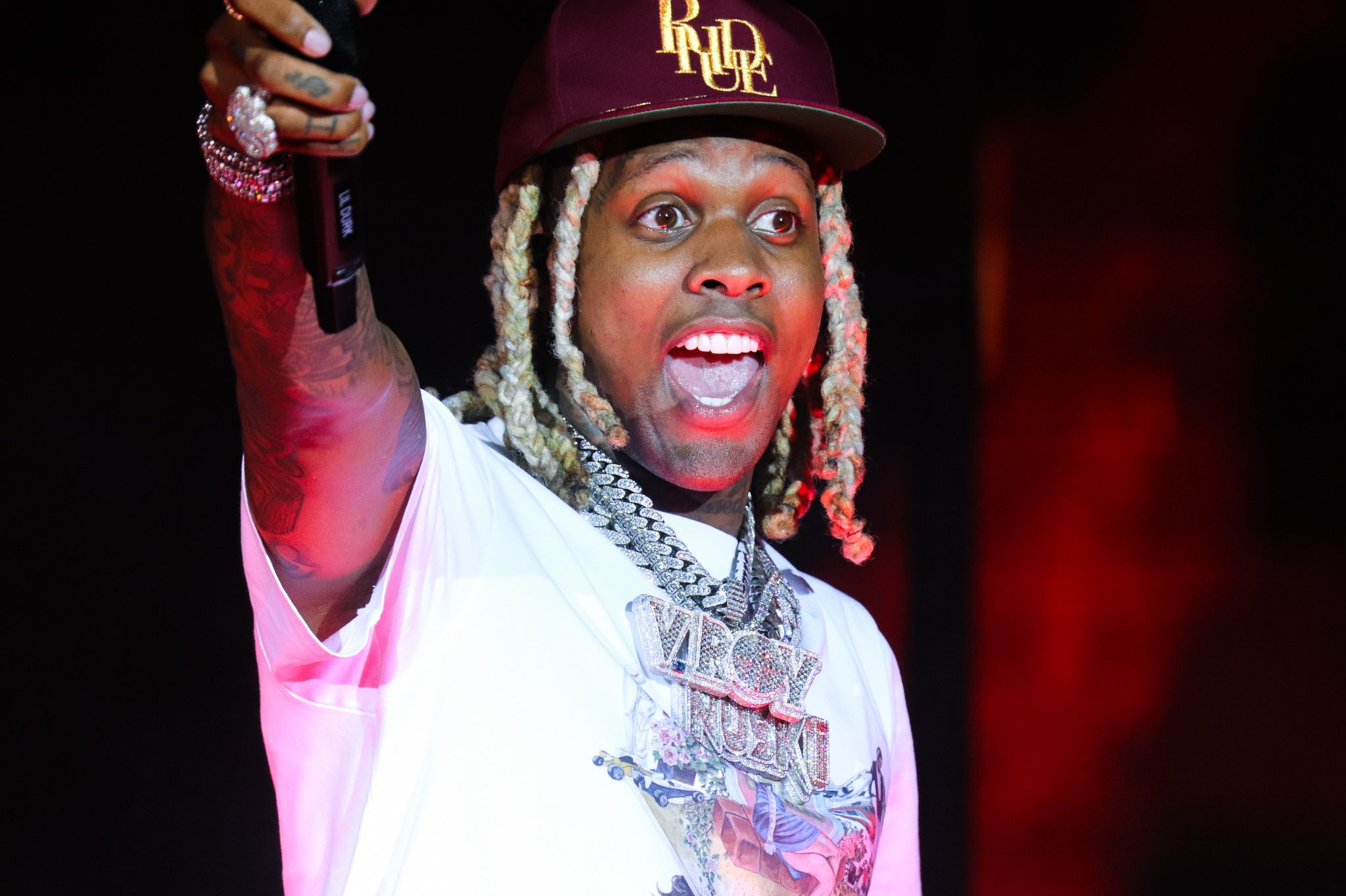 Performer in baseball cap and chains gestures while singing during live concert.