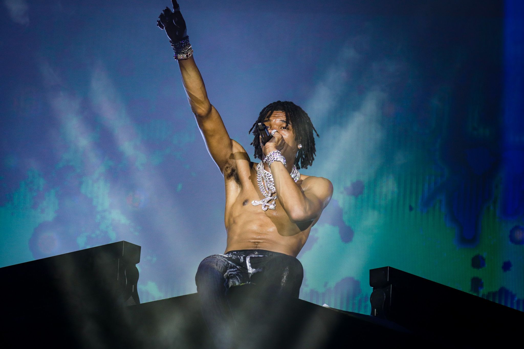 Shirtless performer raises arm triumphantly during dramatic concert with blue and green lighting effects.