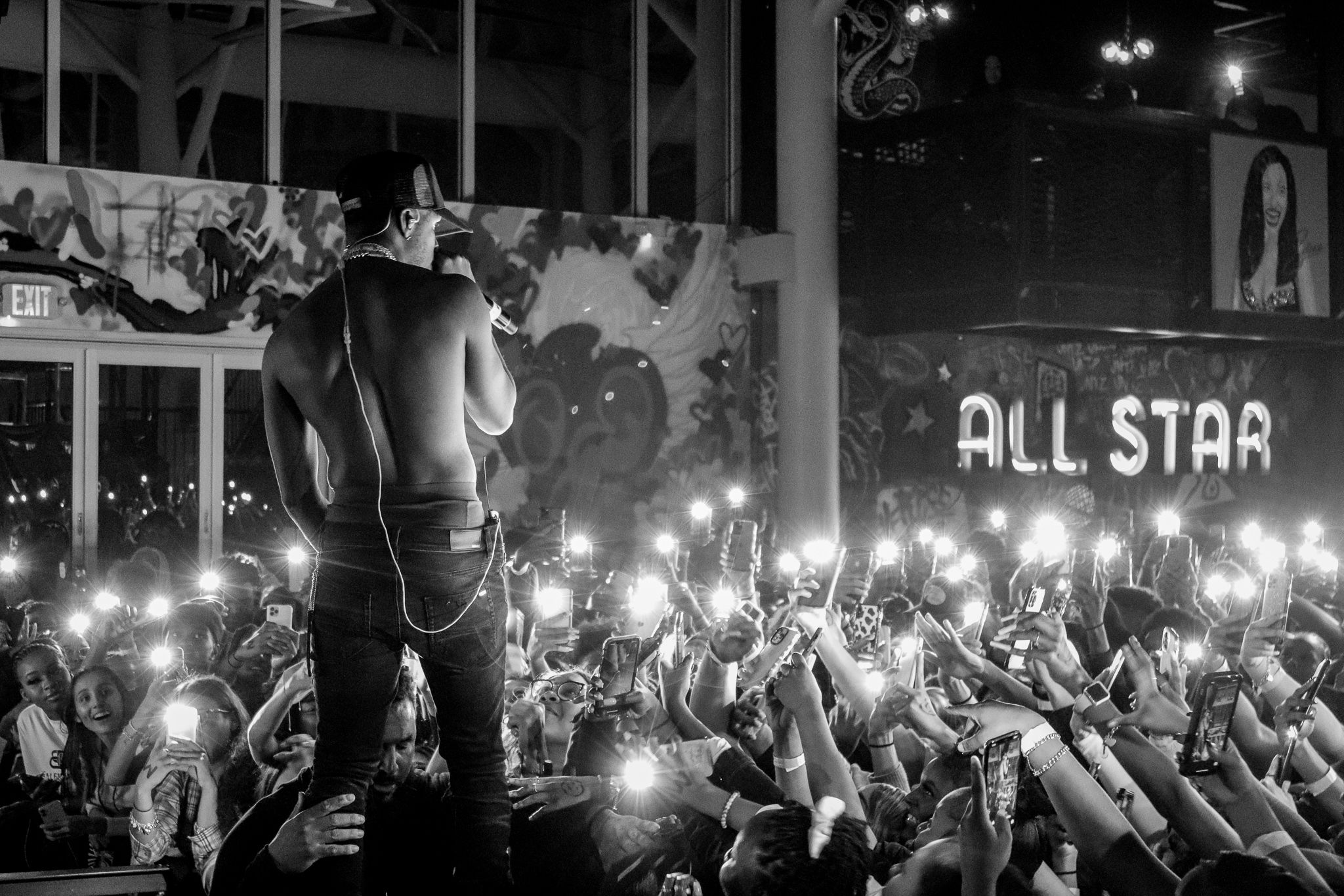 Concert crowd holding up phone lights at night while performer stands on stage.