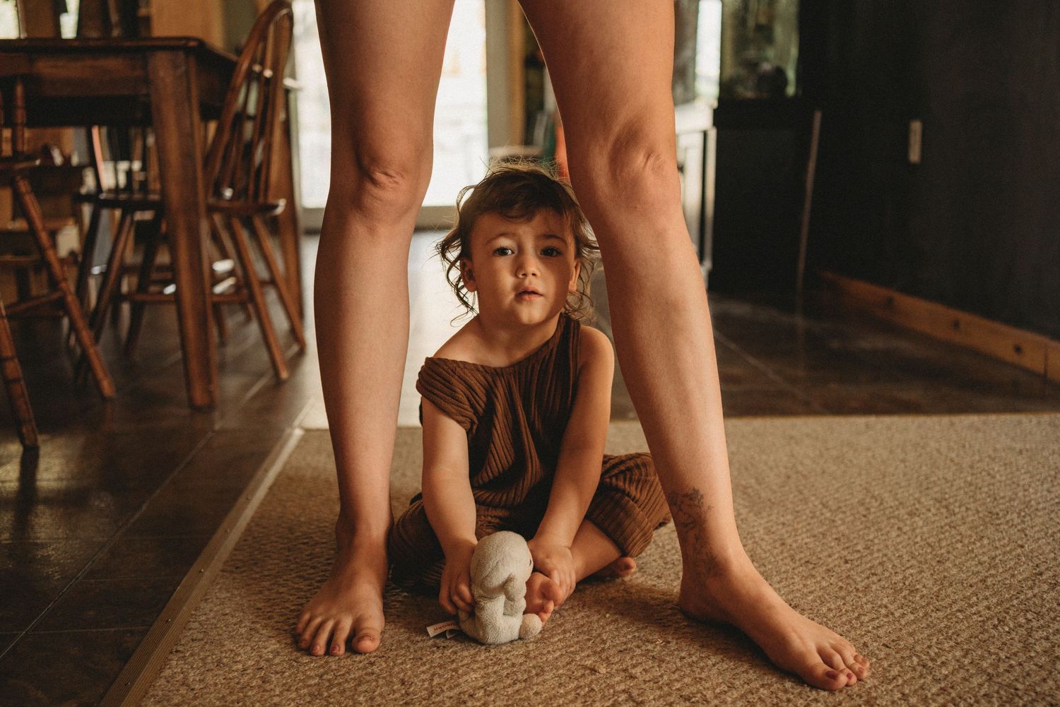 Playful candid moment of child crawling beneath legs in home setting.