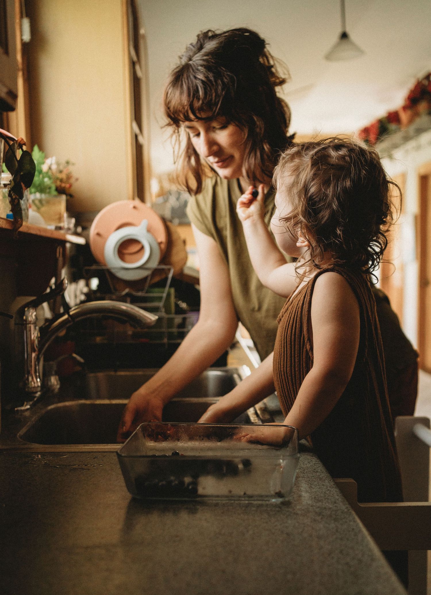 Kitchen scene with parent and child washing dishes together in warm lighting.