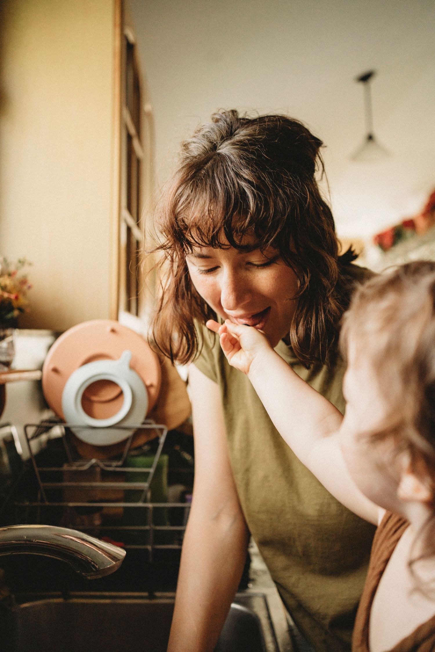 A warm candid kitchen moment shows someone feeding a bite of food while holding a jar.