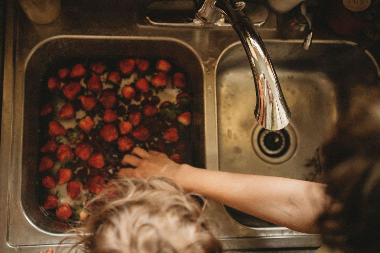 Fresh strawberries being washed in a stainless steel kitchen sink.