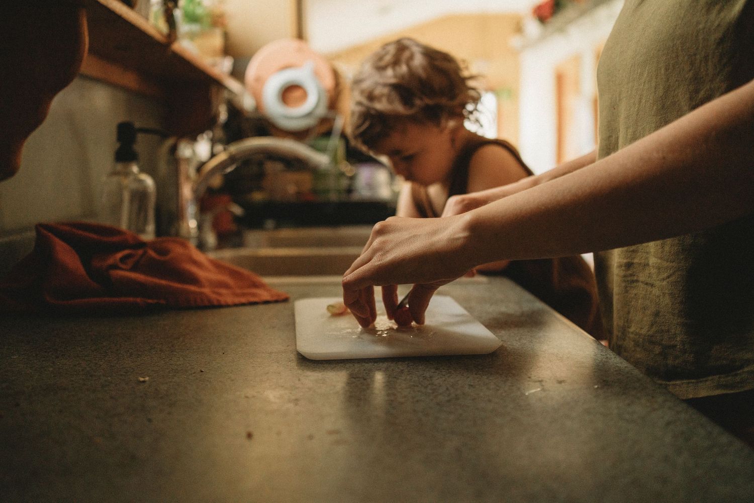 Someone chopping ingredients on a wooden cutting board in warm kitchen lighting.