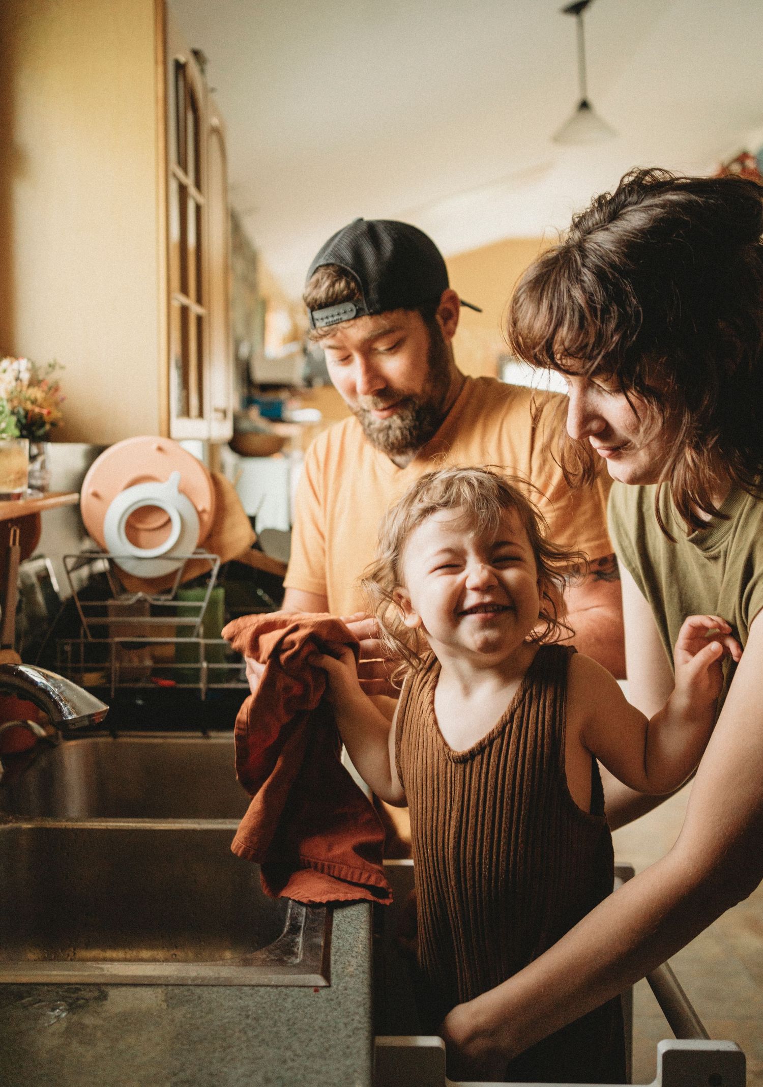Family sharing a joyful moment while doing dishes together in a sunlit kitchen.