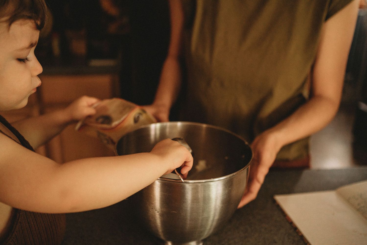 Small hands reaching into a metal mixing bowl during food preparation.