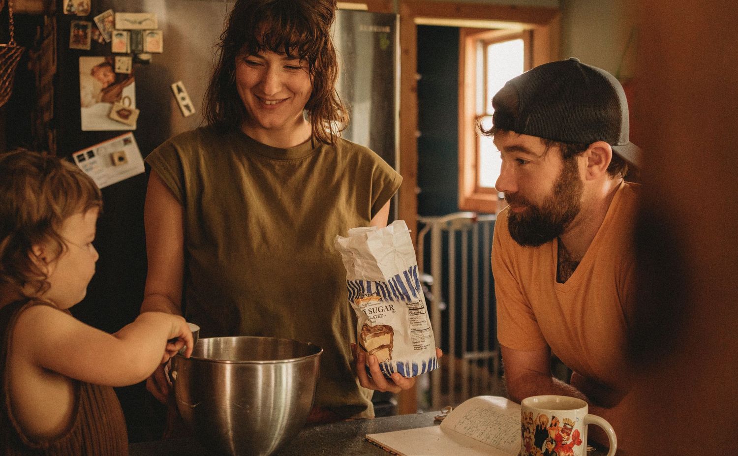 A family bakes together in the kitchen, adding ingredients to a mixing bowl on a cozy afternoon.