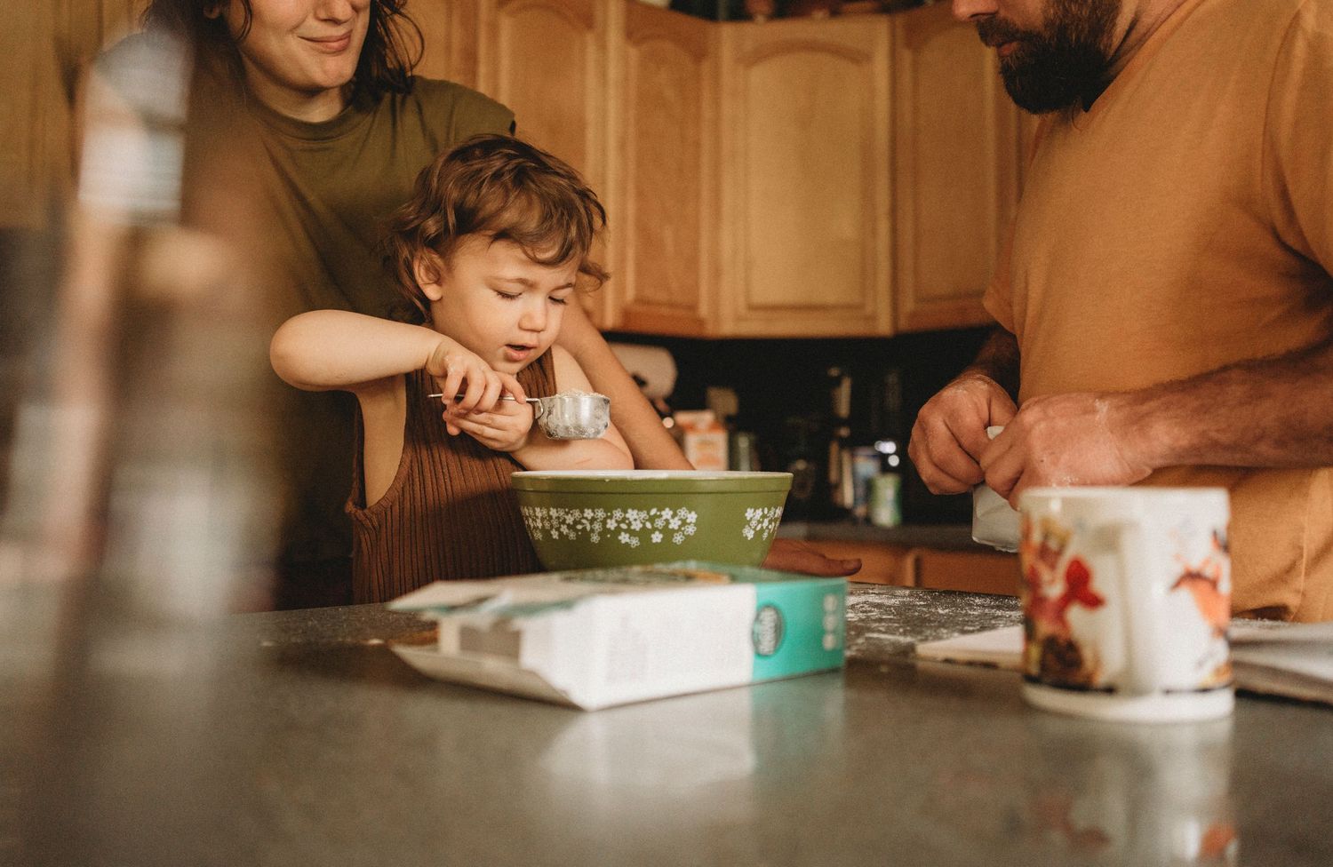 A family gathering around a mixing bowl in the kitchen during a baking session.