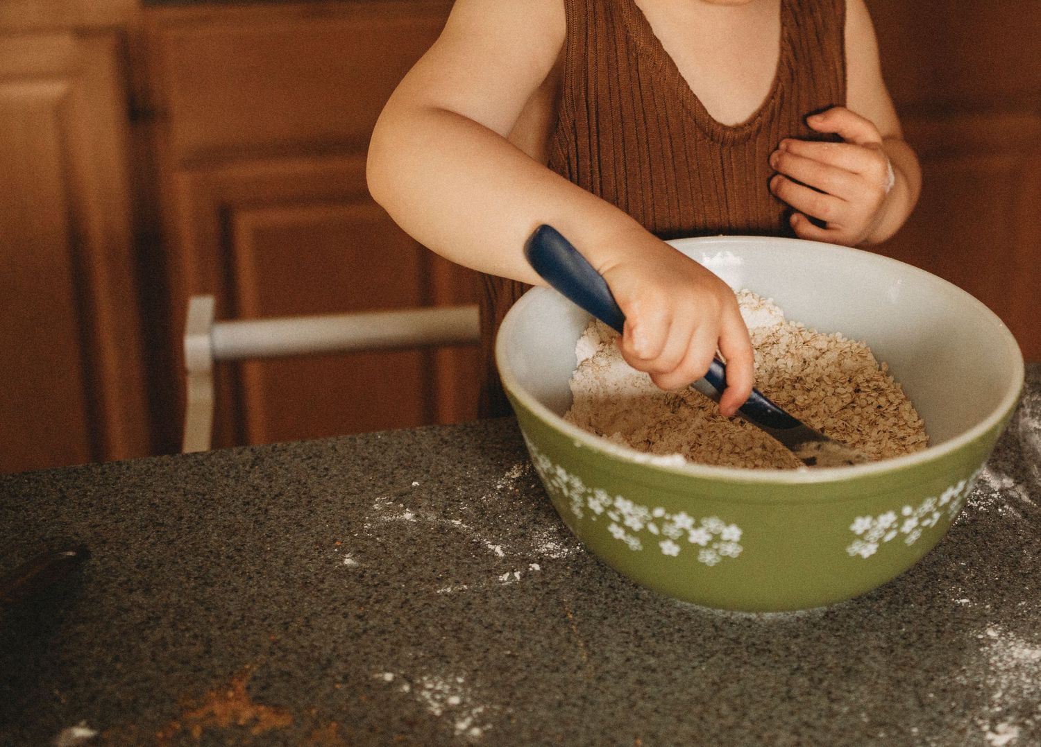 Hands stir ingredients in a decorative green and white mixing bowl on a flour-dusted countertop.