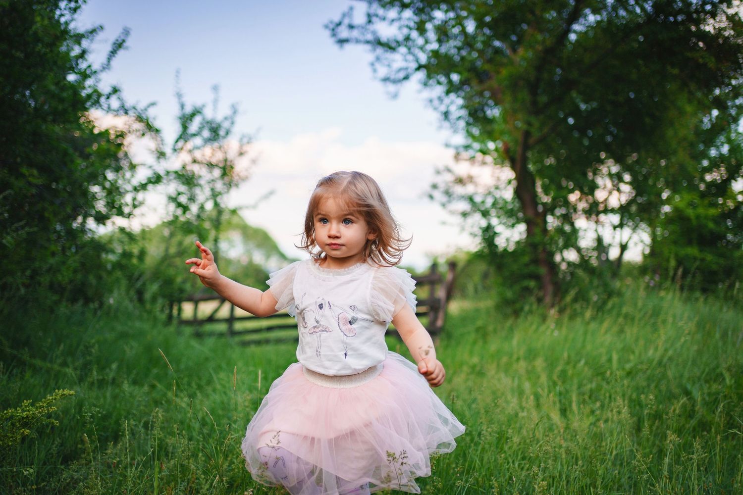 A young dancer spins in a pink tulle dress in a grassy field during golden hour.