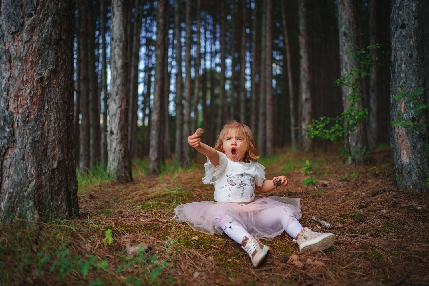 A young dancer in a tutu dress performs gracefully on a forest trail between tall trees.