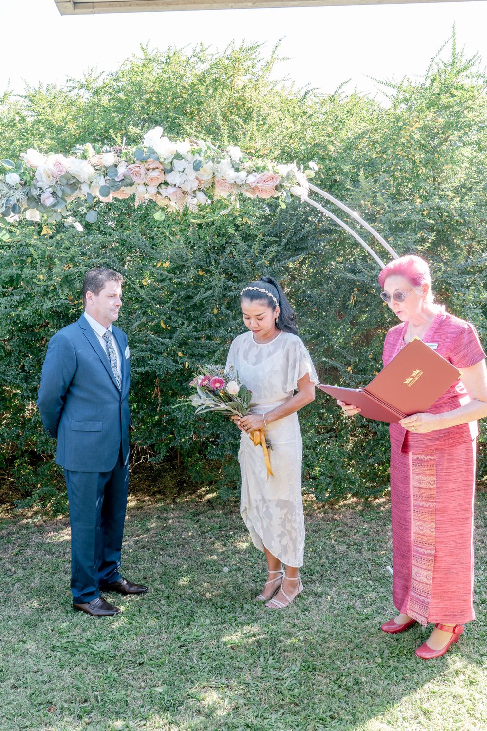 elopement ceremony bride and groom with celebrant in pink tones decorated arbour