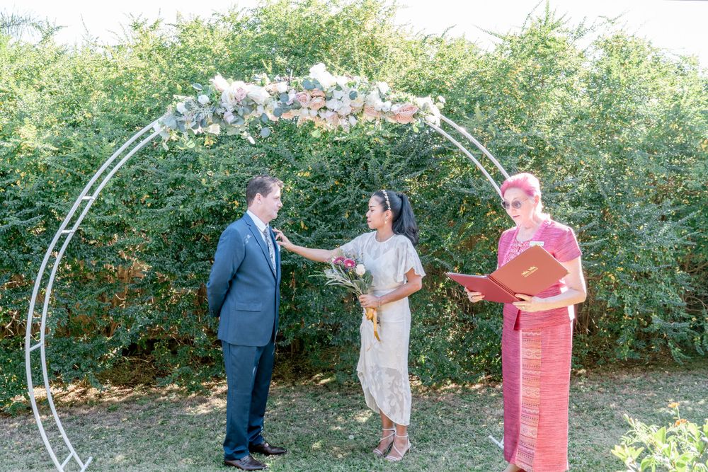 Wedding ceremony setup with white arch and chairs in an outdoor garden setting.
