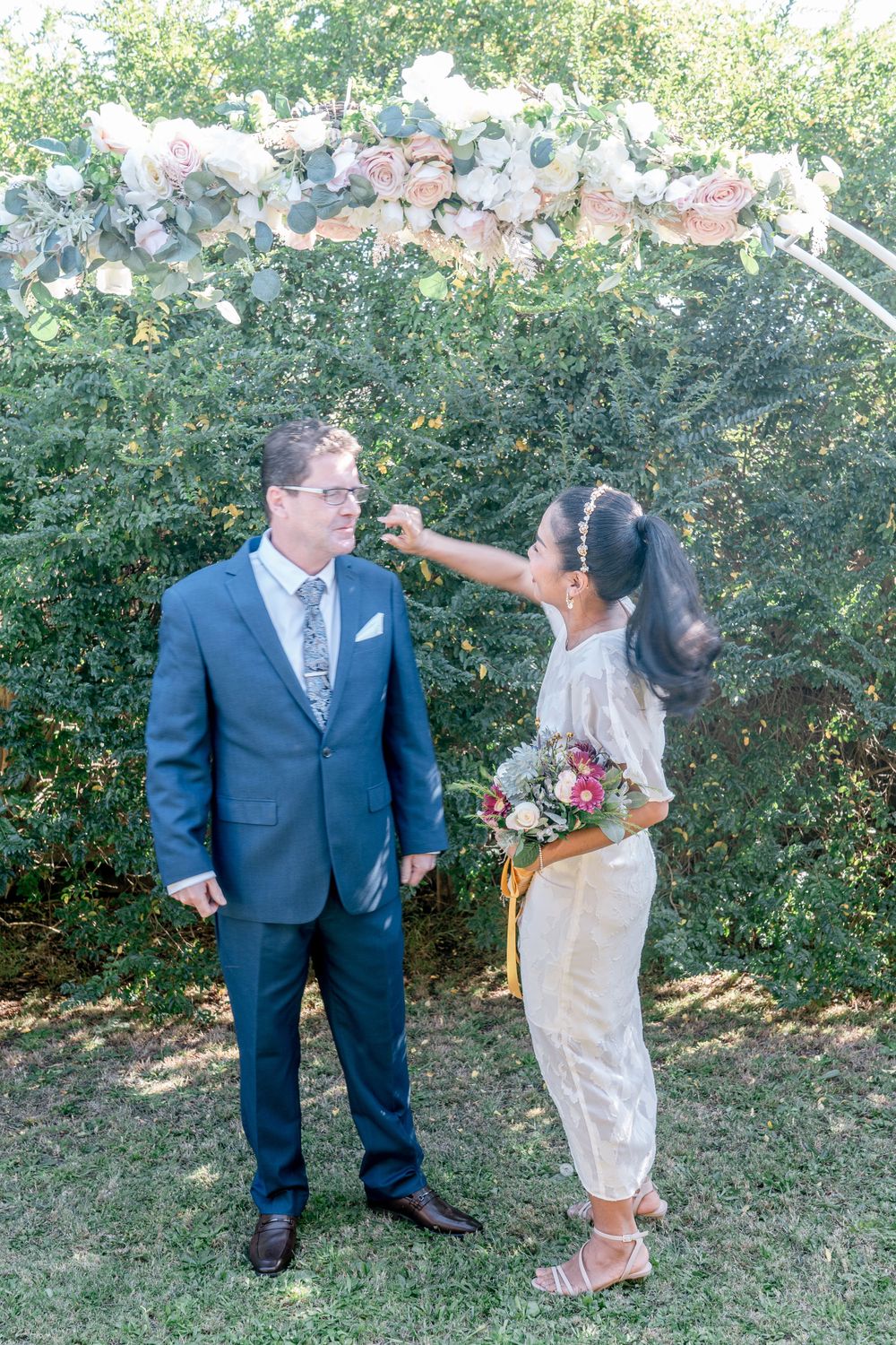 aisan bride tenderly wiping lipstick off mature groom after first kiss elopement backyard