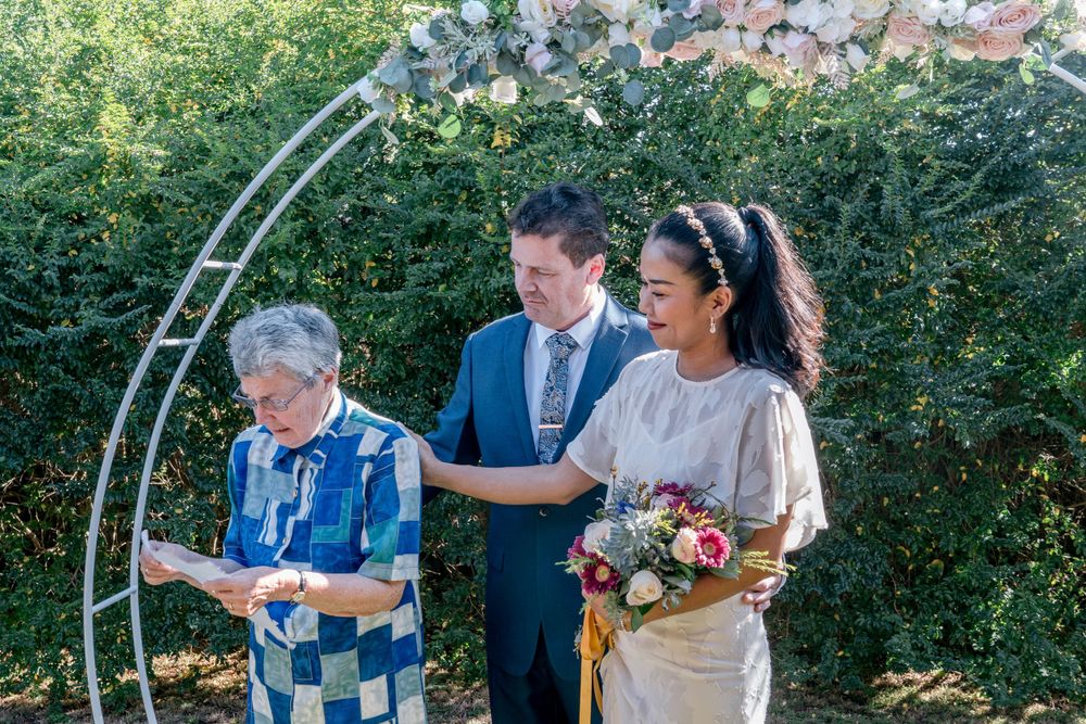 elderly woman in blue dress reading wedding blessing while bride and groom cry and comfort her