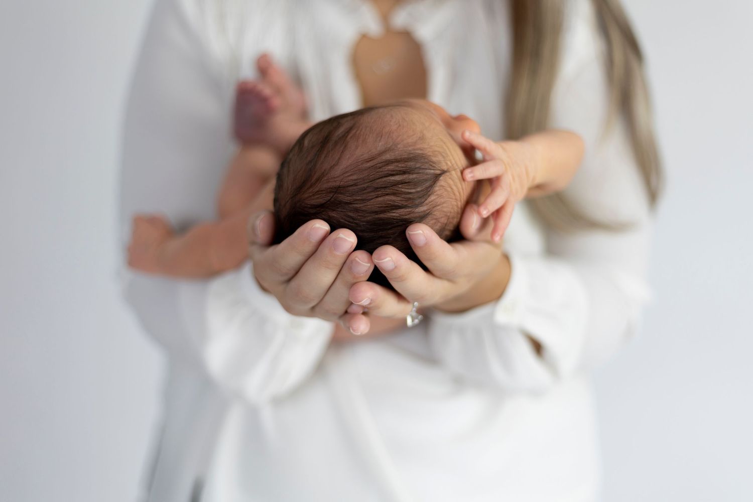 Baby cradled gently in caregiver's hands with soft white clothing.