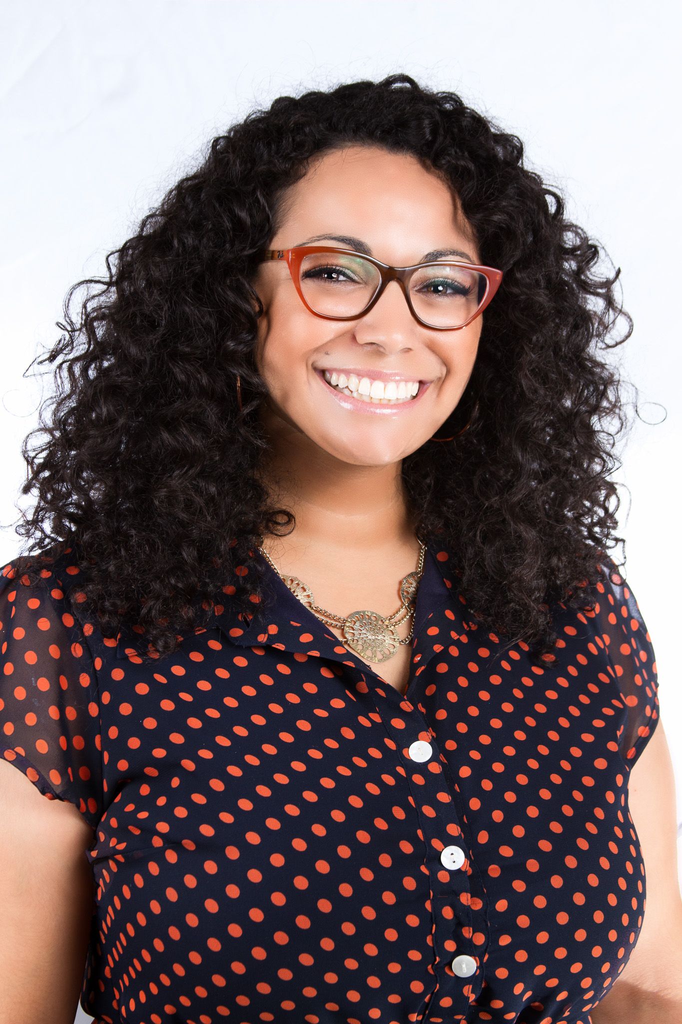 Professional portrait series showing bright smile and curly hair wearing polka dot top and glasses.