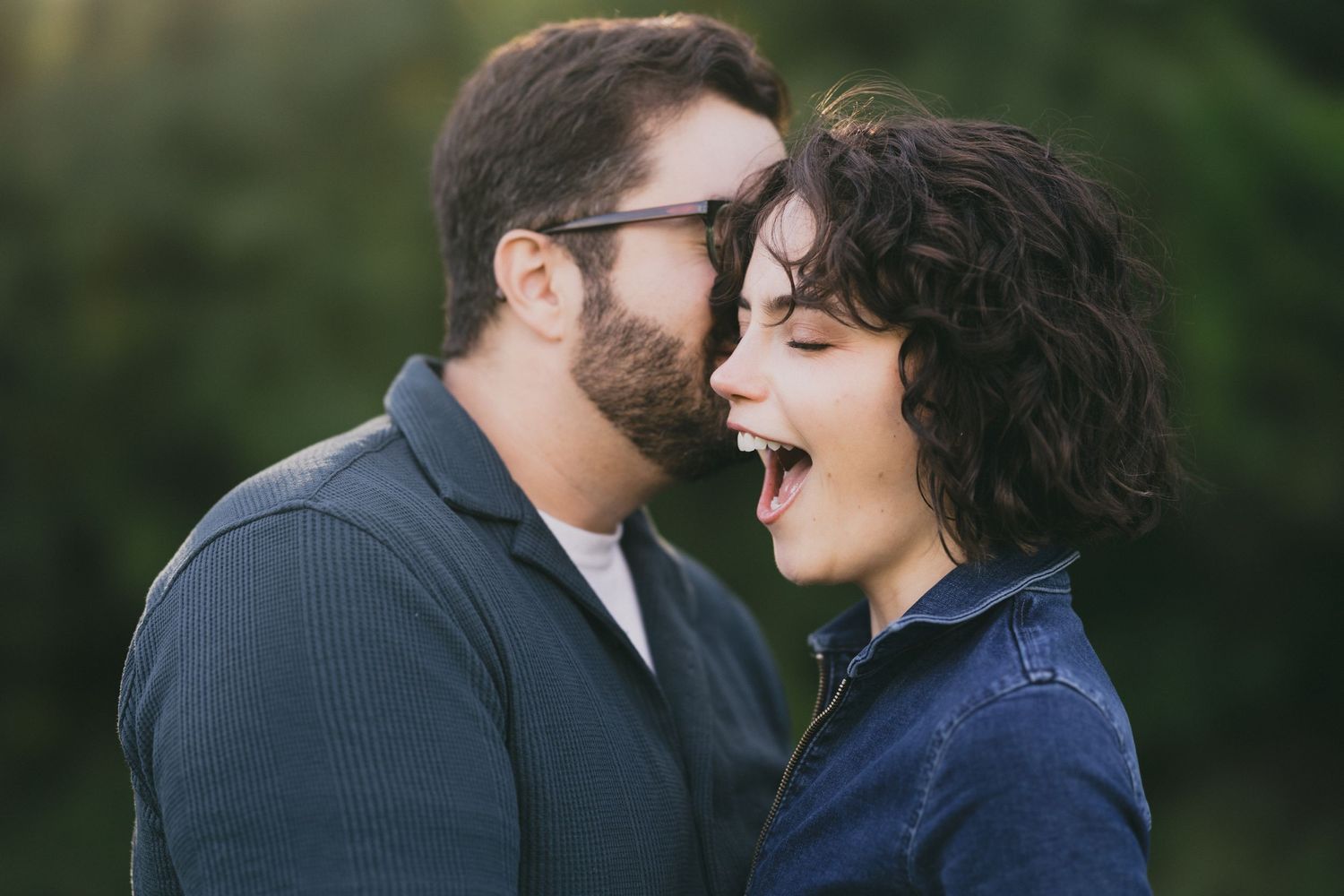 A couple shares a joyful laugh together outdoors in a candid romantic moment.