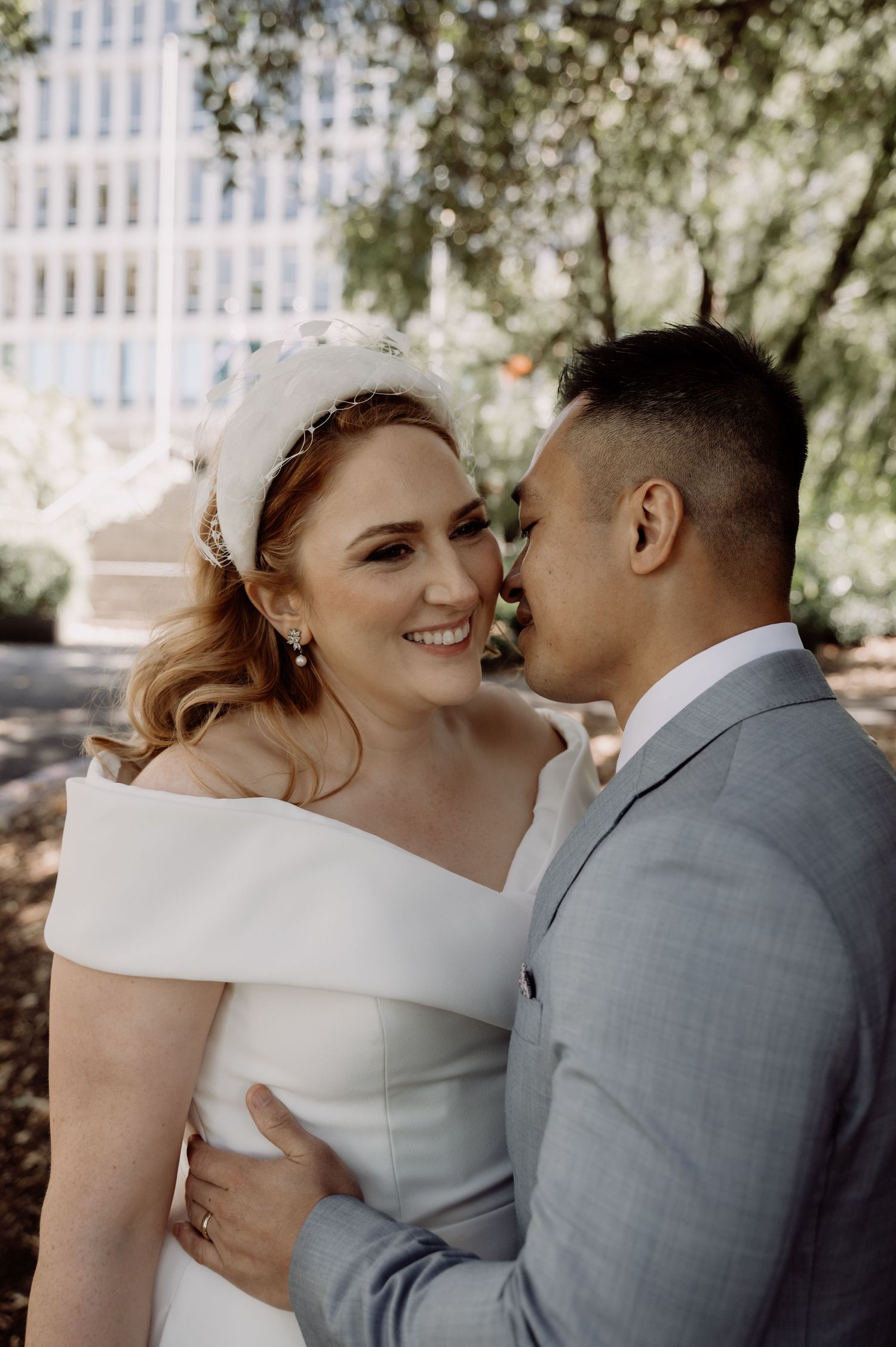 A tender moment captured between a bride in white and groom in grey during an outdoor wedding photo session.
