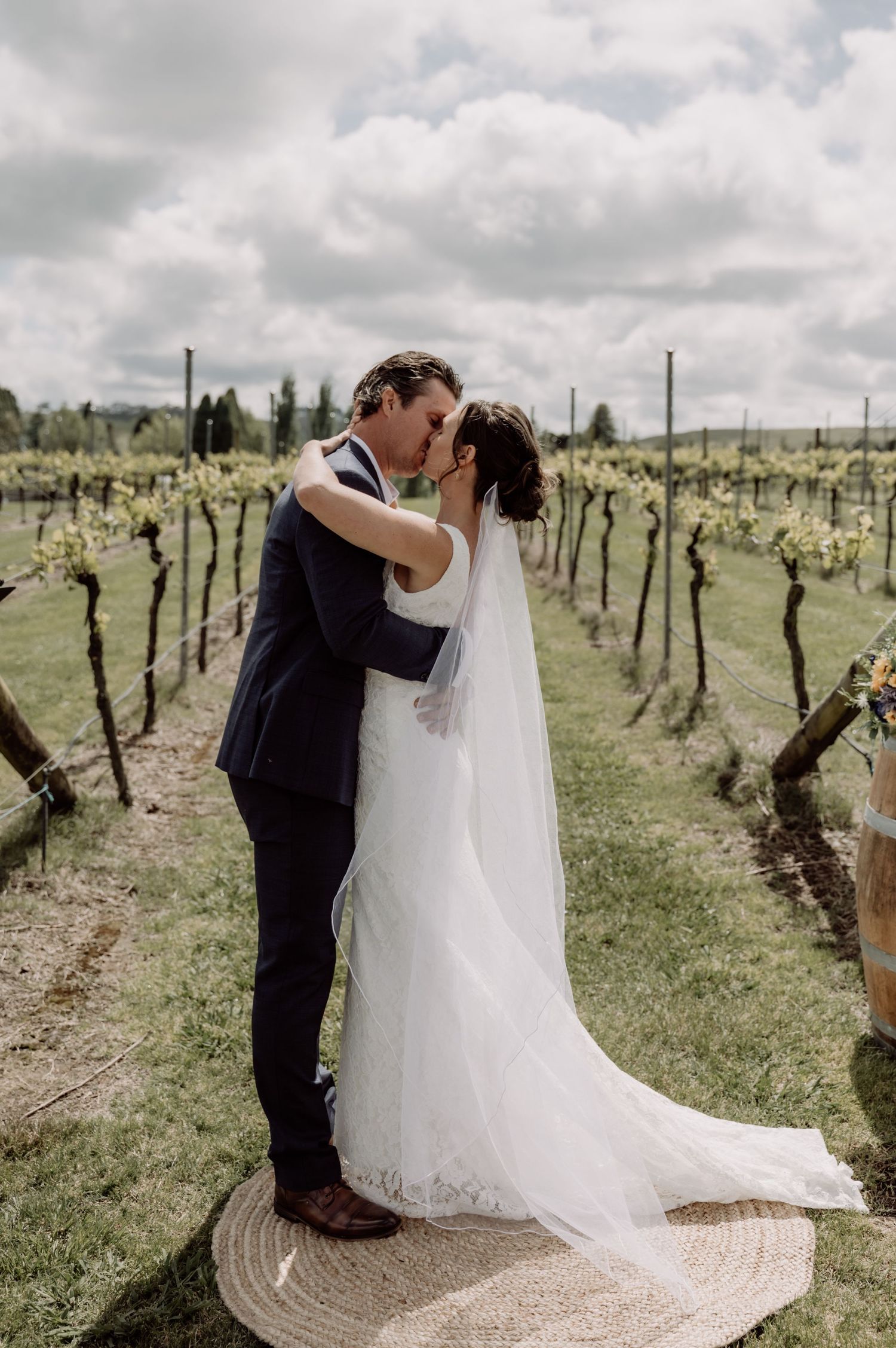 A romantic wedding photo of a couple embracing in a scenic vineyard on a cloudy day.