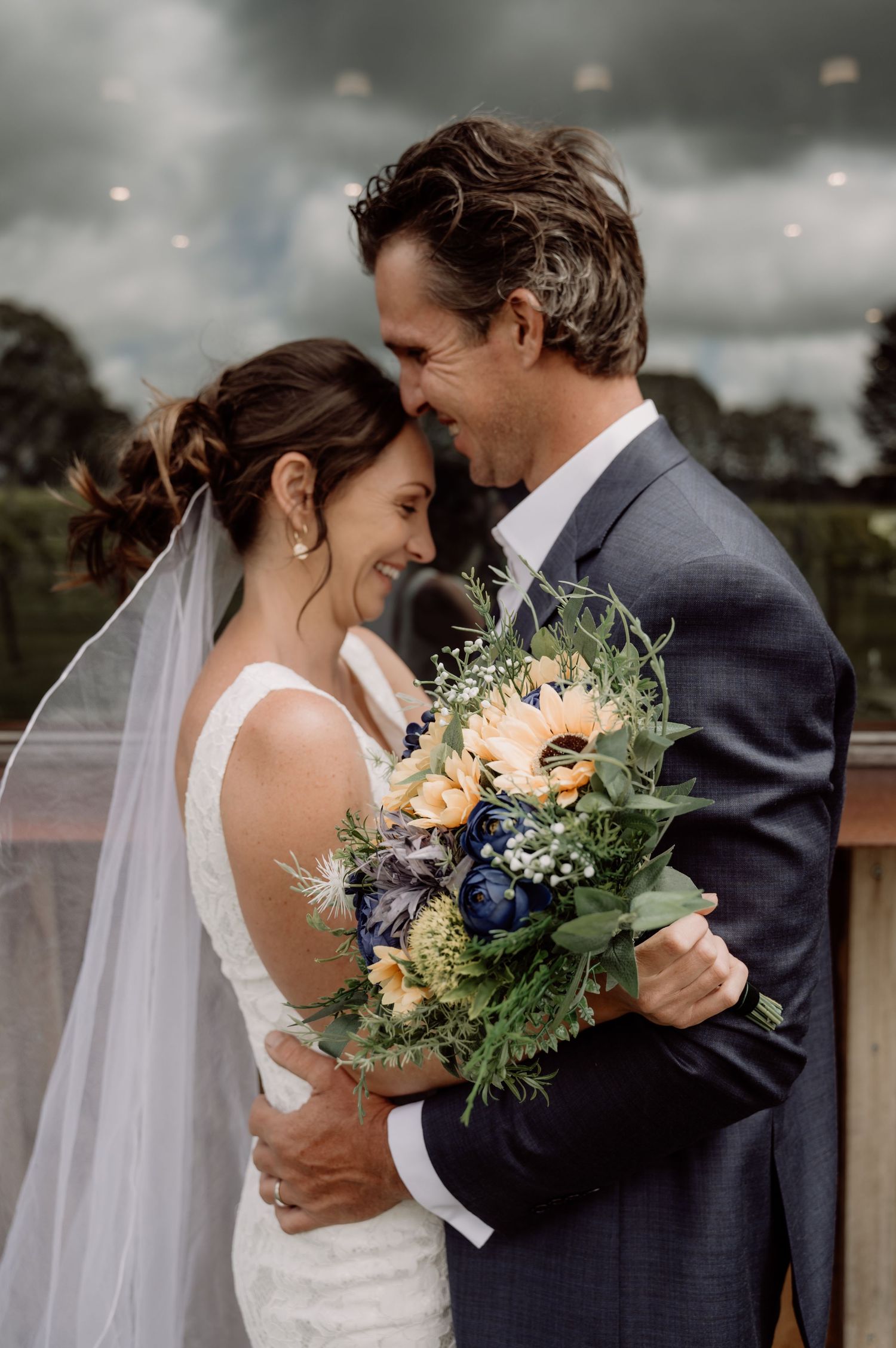 A romantic wedding moment between a couple with a beautiful bouquet of peach and navy flowers against a moody sky.