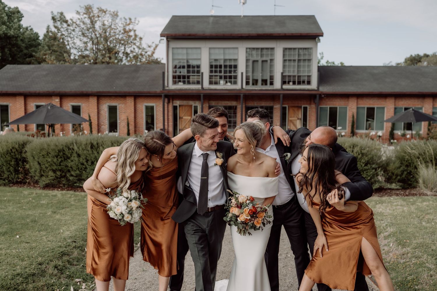 Wedding party wearing brown and white attire stands together in a casual outdoor setting during autumn season.