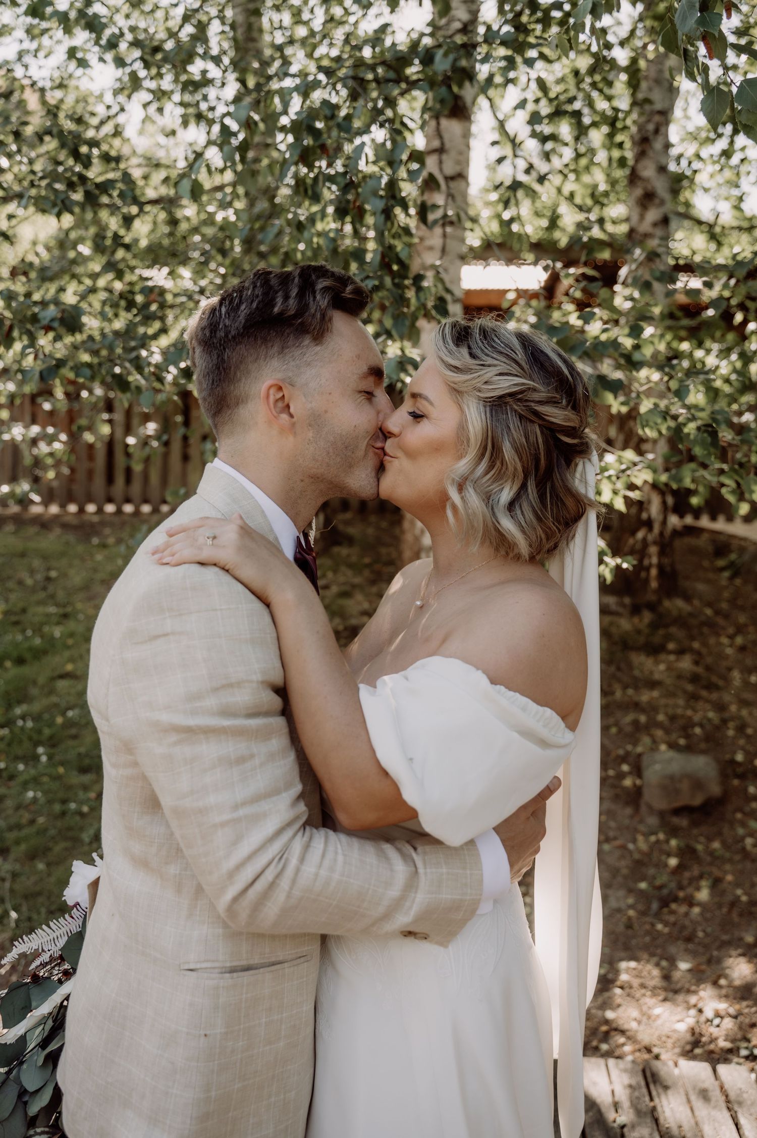 A couple shares an intimate moment in a garden setting on their wedding day, wearing light colored attire.