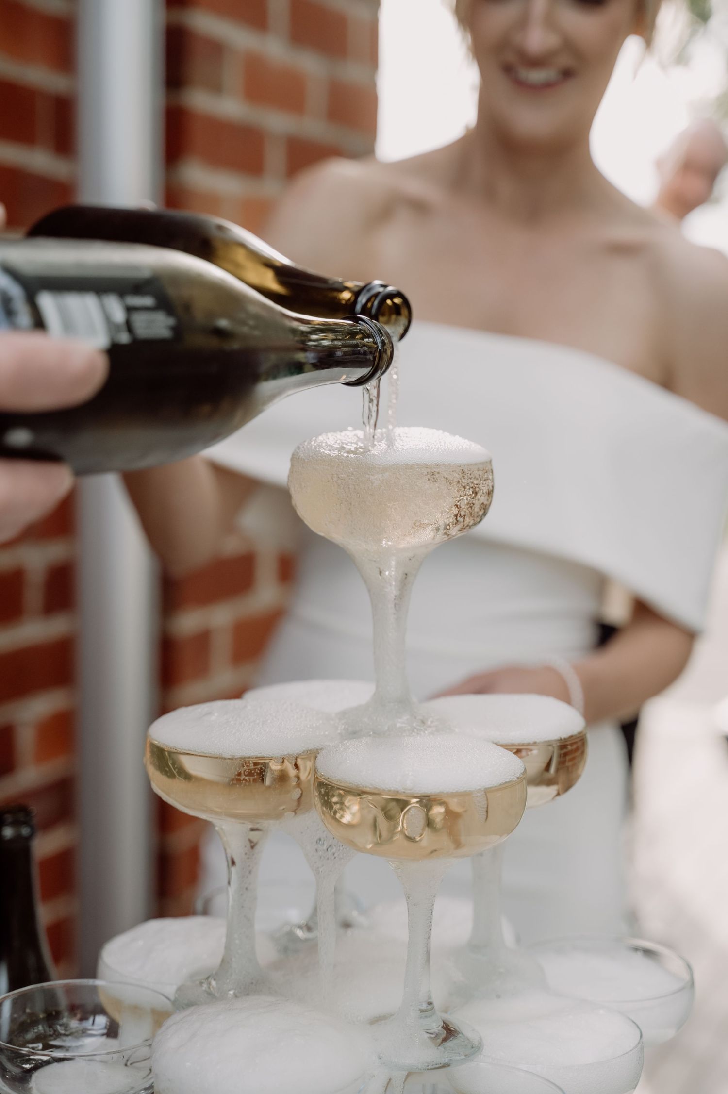 Champagne being poured into a tower of elegant coupe glasses creating a cascading fountain effect at a celebration.