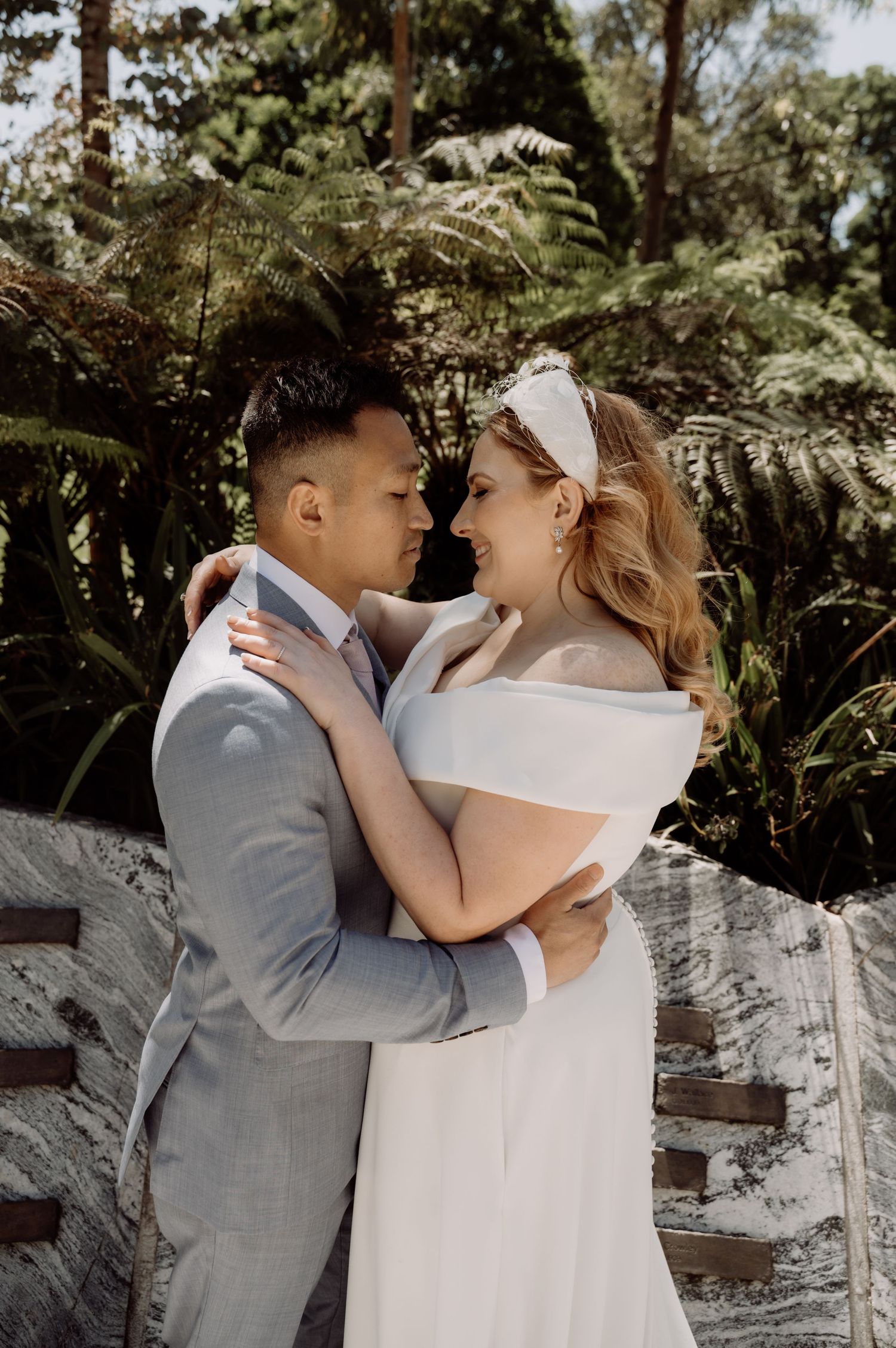 A romantic couple embraces in an intimate moment surrounded by lush ferns and tropical greenery in the afternoon light.