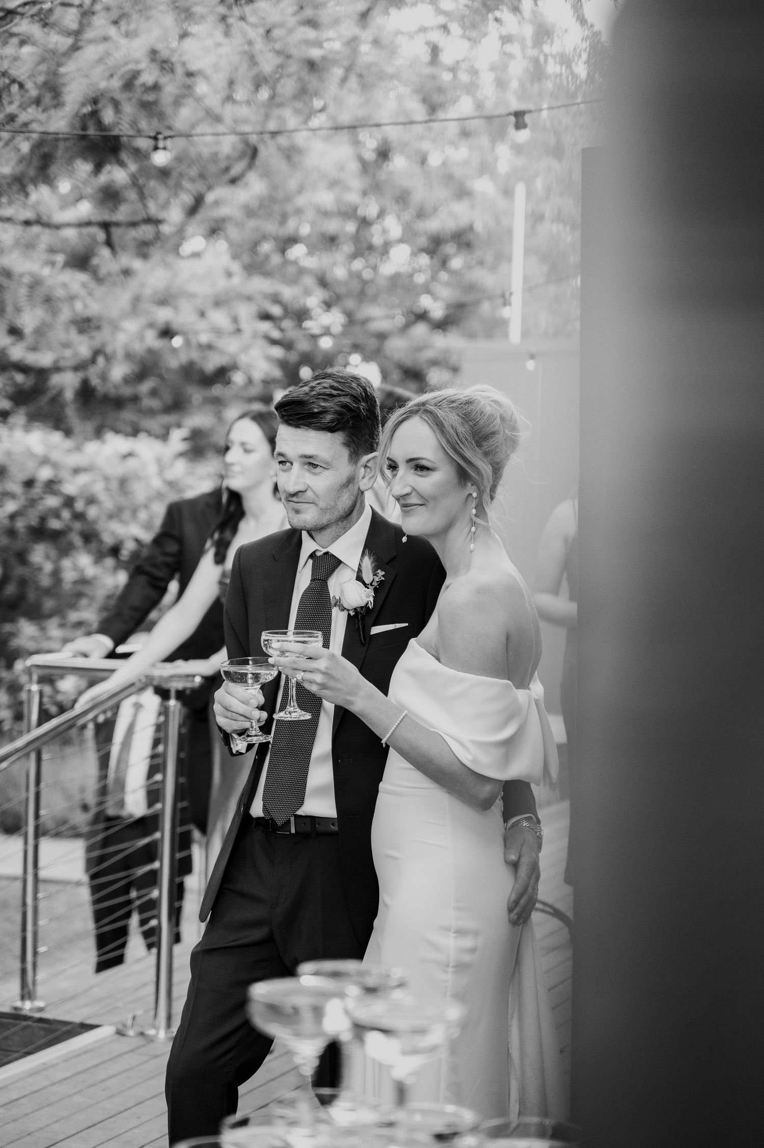 Black and white photo of a couple in formal wedding attire sharing a laugh together on a garden terrace.