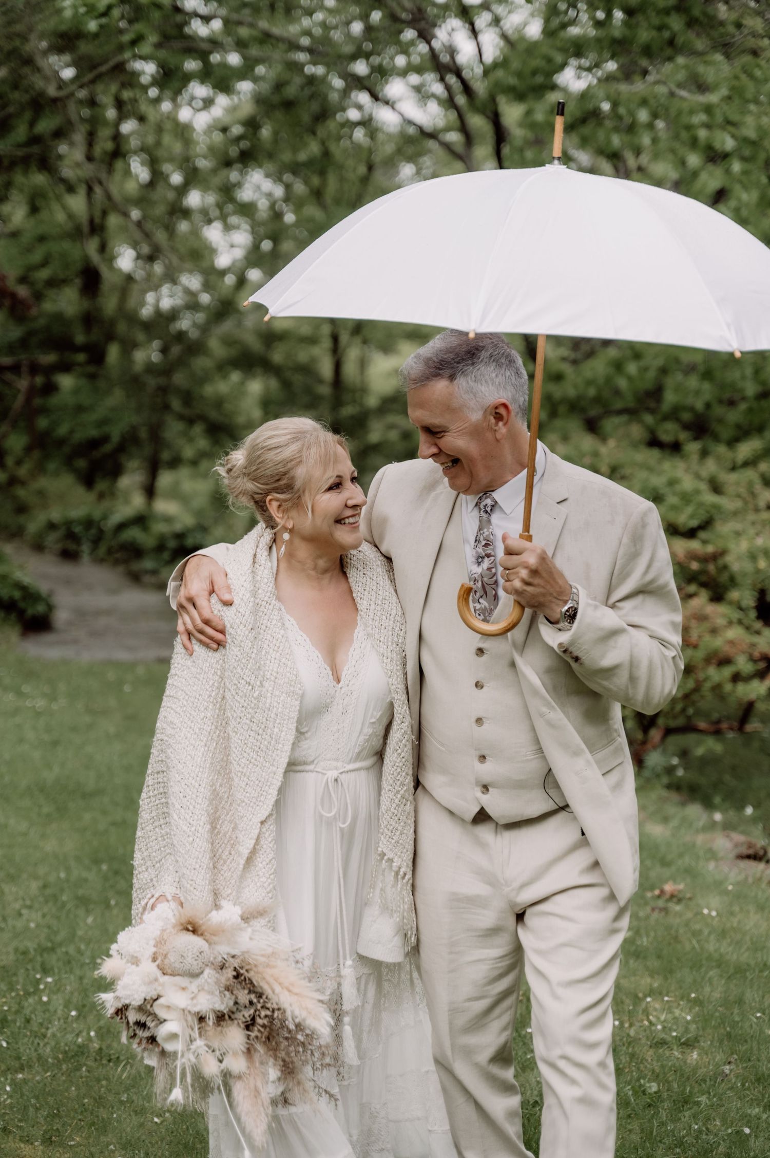 A happy couple shares a joyful moment under a white umbrella during their outdoor wedding celebration.
