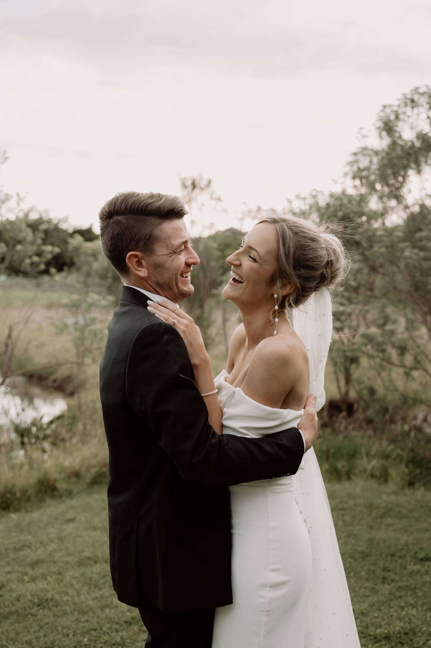 A romantic outdoor wedding moment as a couple embraces and laughs joyfully in a natural setting with greenery.