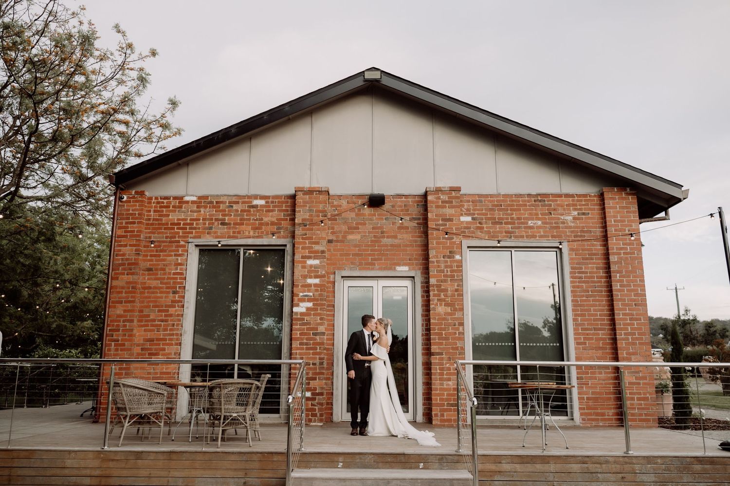 Couple stands outside modern brick building with glass windows and outdoor patio seating area.