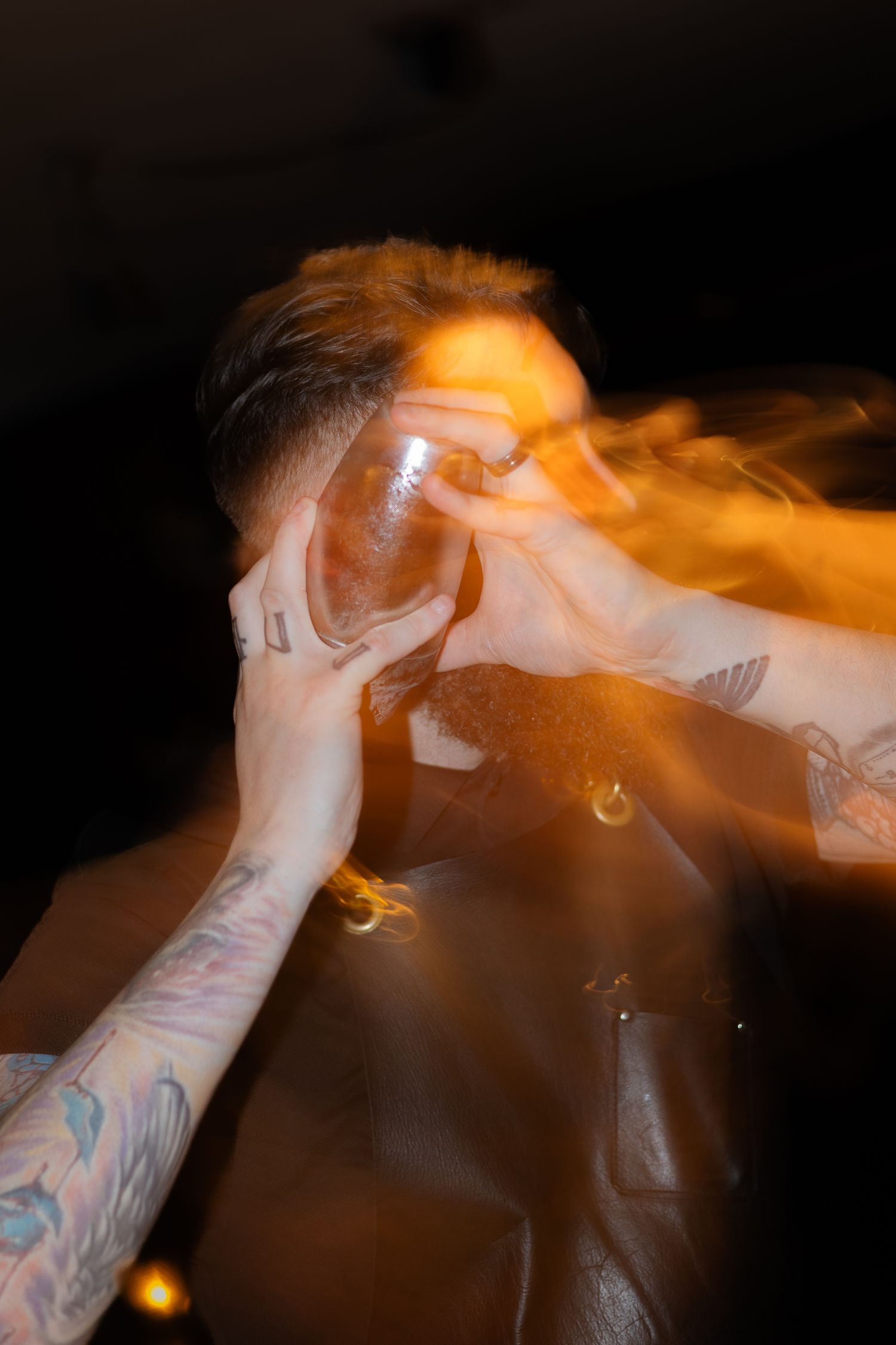 Artistic photo of someone exhaling smoke in orange lighting with visible tattoos.