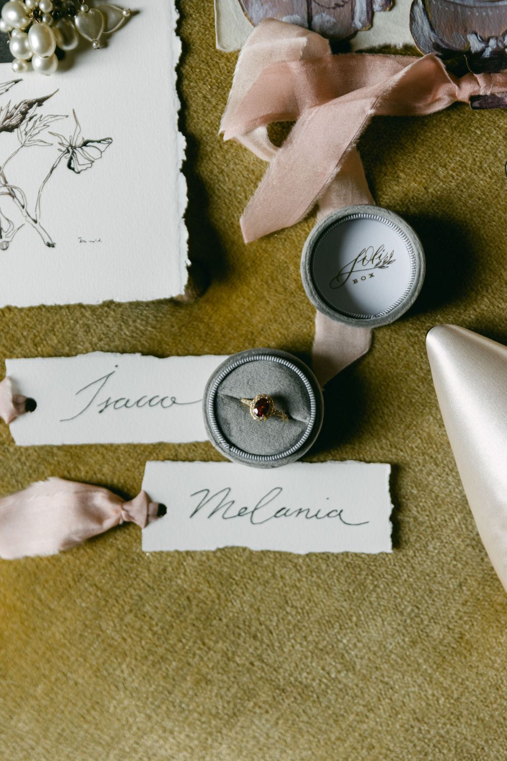 Wedding detail shot with handwritten name cards and vintage ring boxes on green velvet.