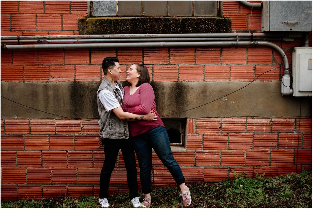 Romantic moment against brick wall with couple in casual attire embracing each other.
