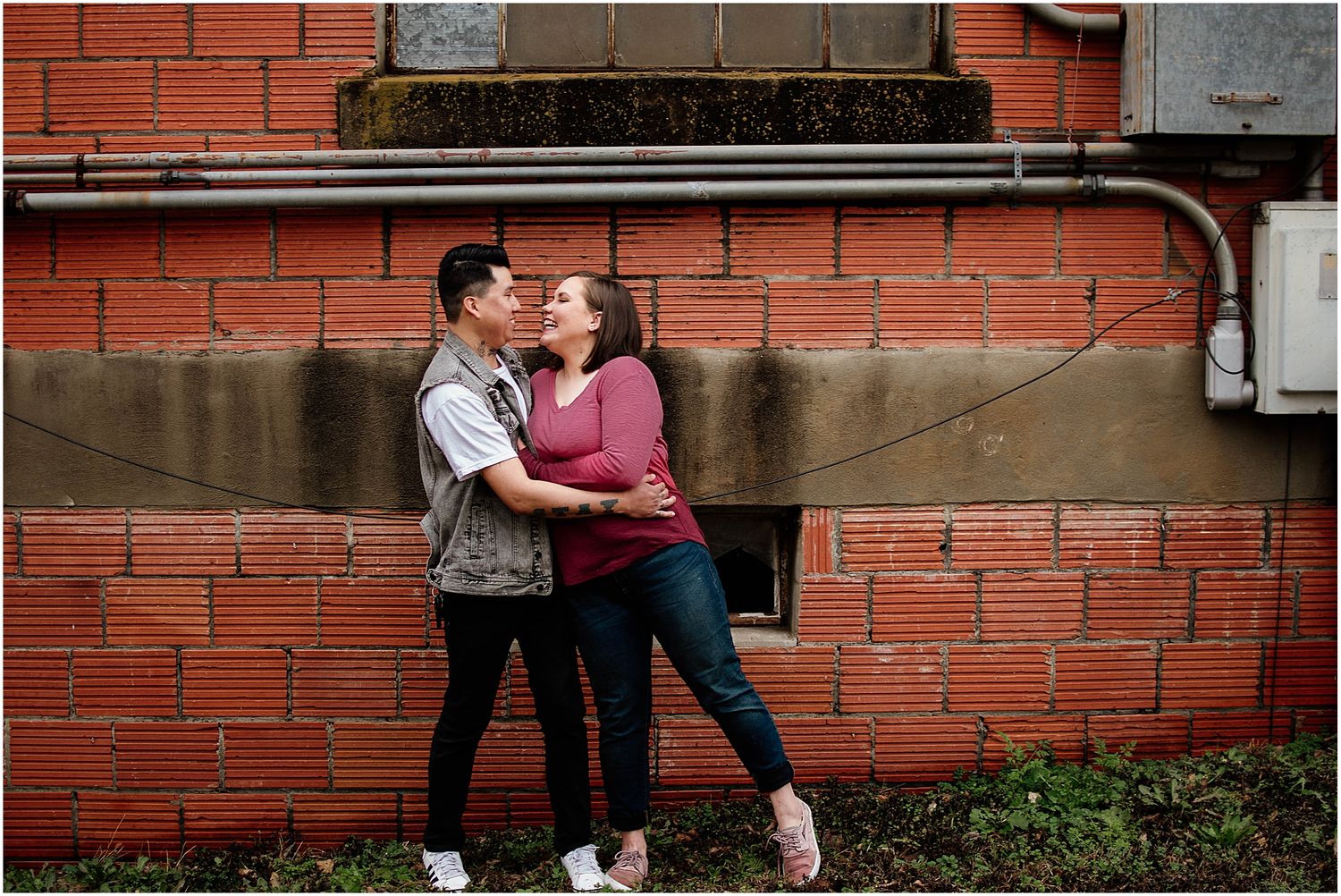 Romantic moment against brick wall with couple in casual attire embracing each other.