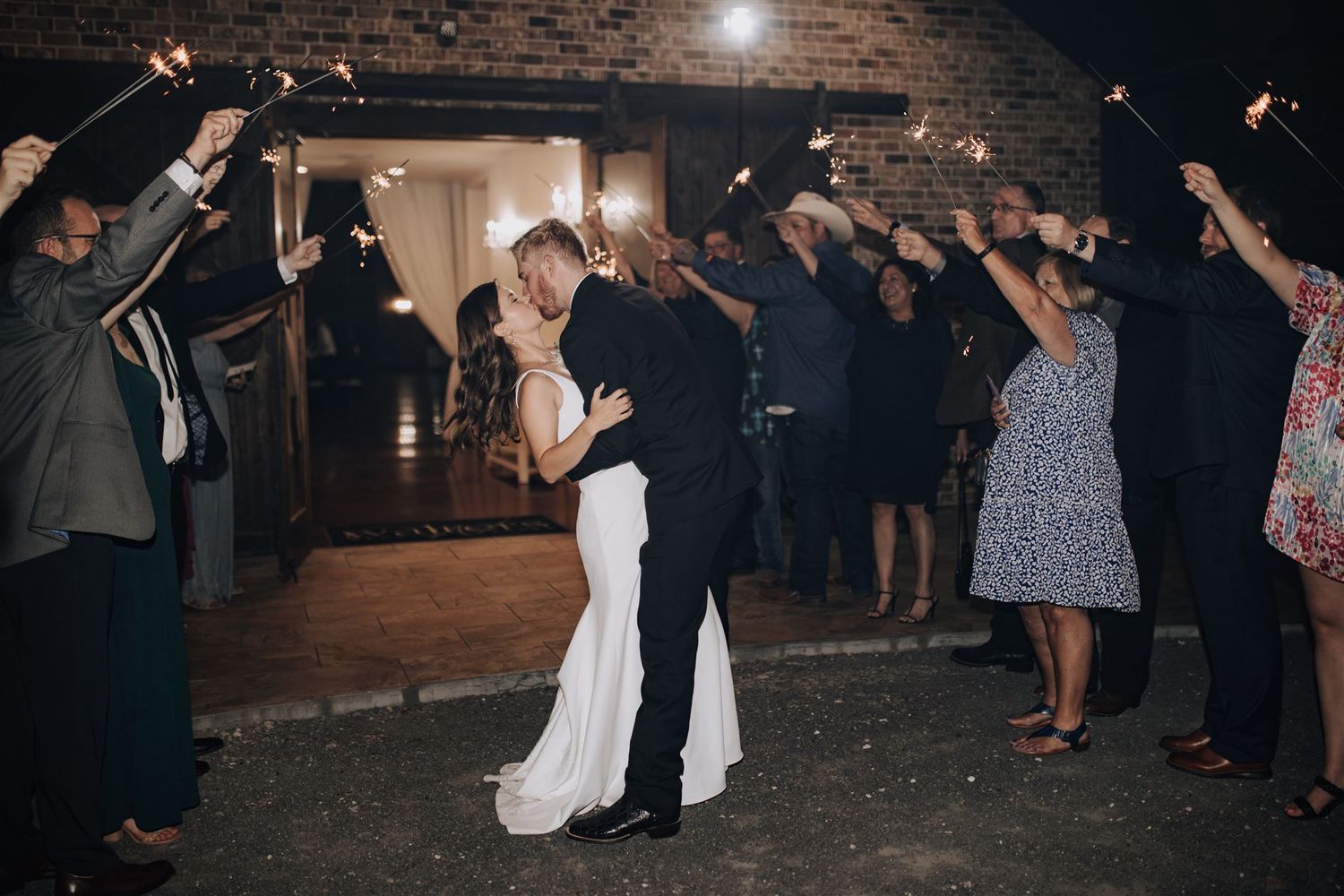 Wedding couple's grand exit under raised arms of guests at brick venue entrance.