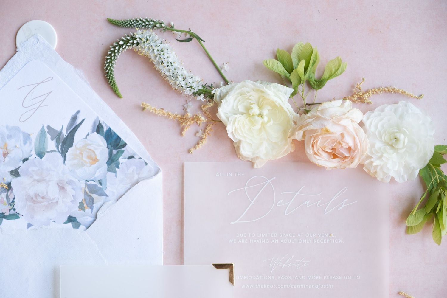 Delicate floral arrangement with white and pink roses alongside wedding stationery on pink background.