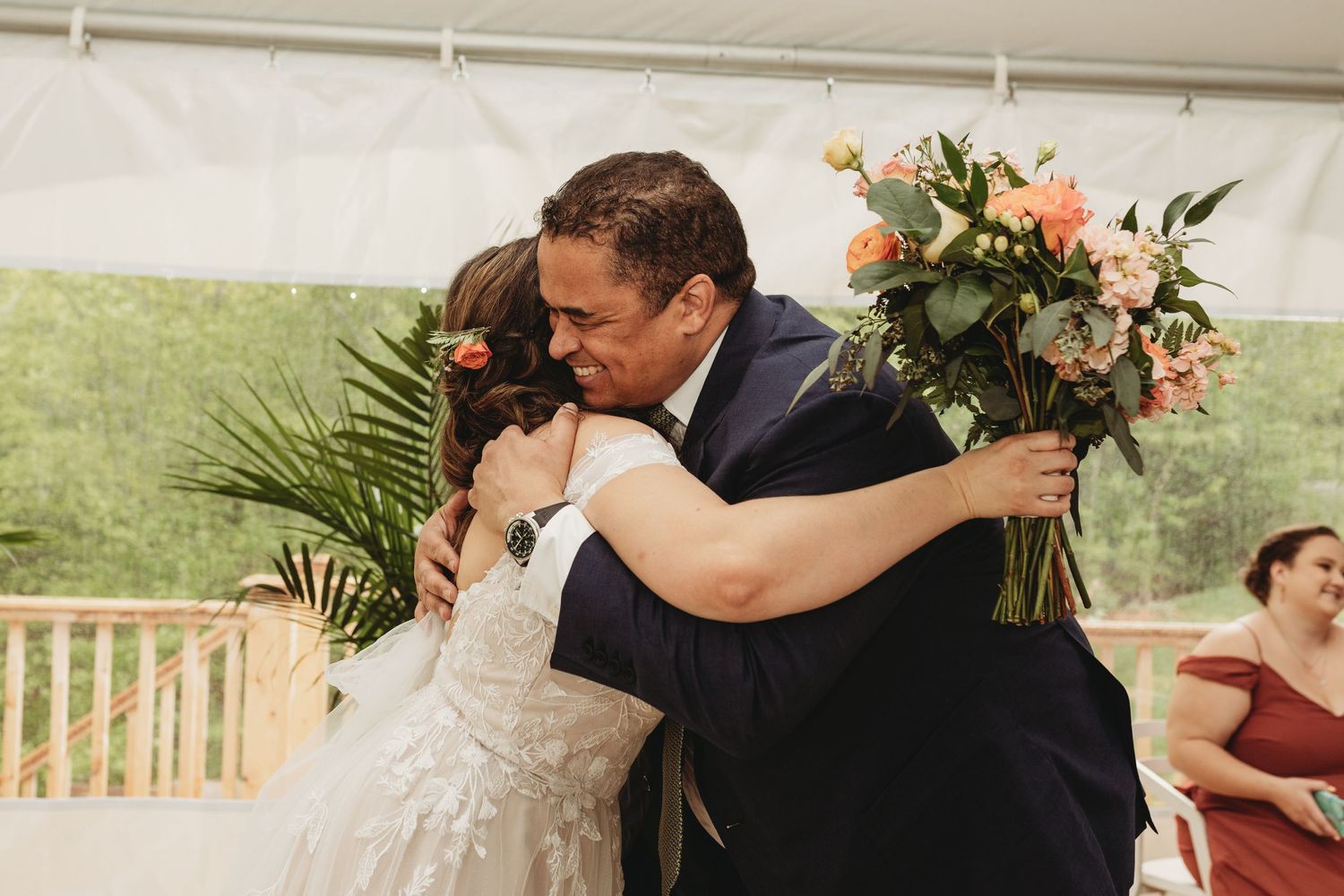 A joyful embrace between a couple during a wedding celebration under a tent with floral arrangements.